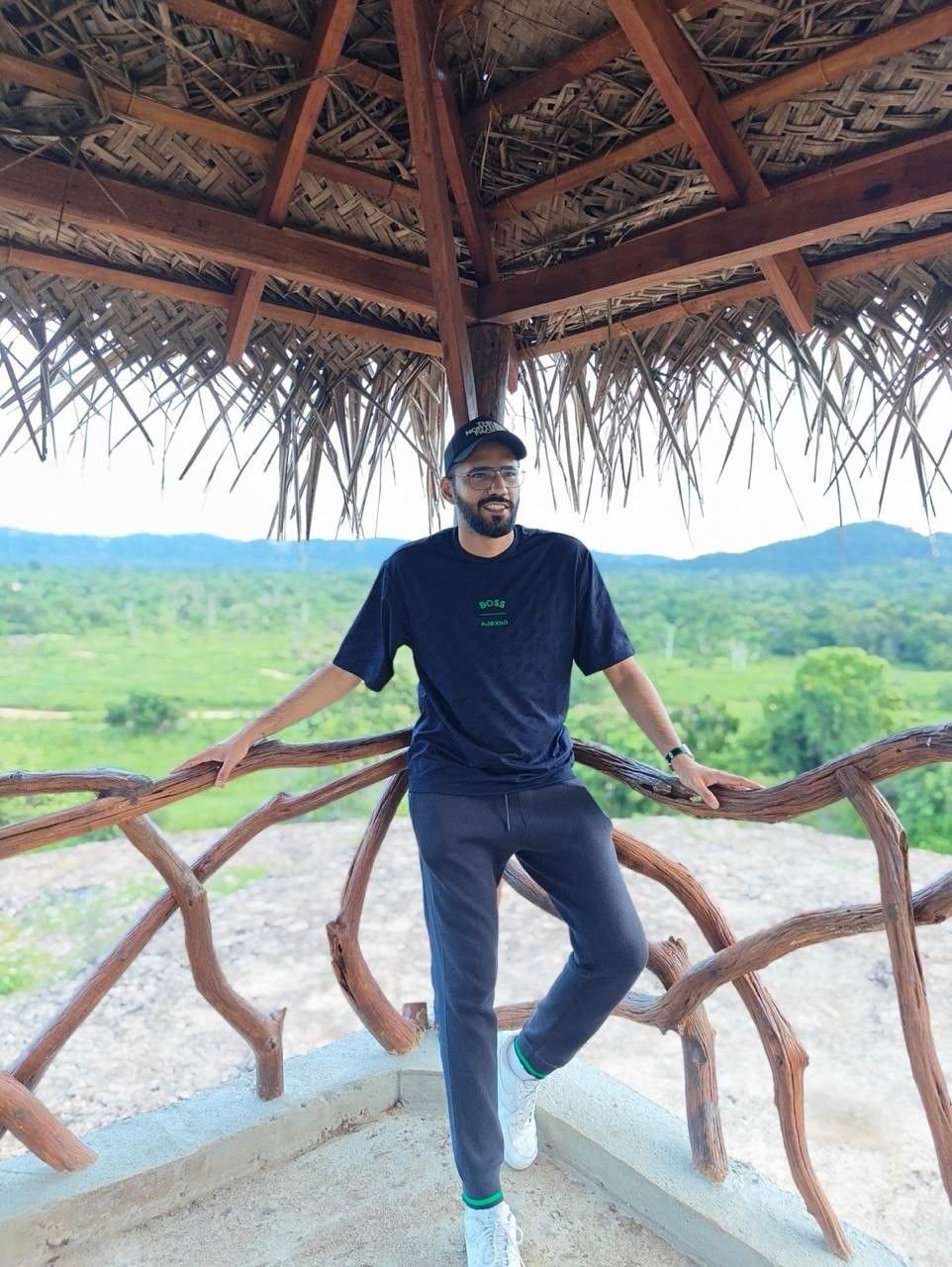 Faaiz leaning on a wooden railing above green hills